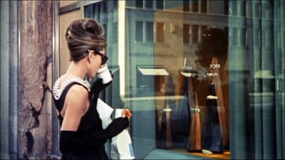 Audrey Hepburn, elegant brand ambassador, in her iconic black Givenchy dress and pearl necklace from "Breakfast at Tiffany's," showcasing the timeless elegance that made her a powerful fashion influencer.
